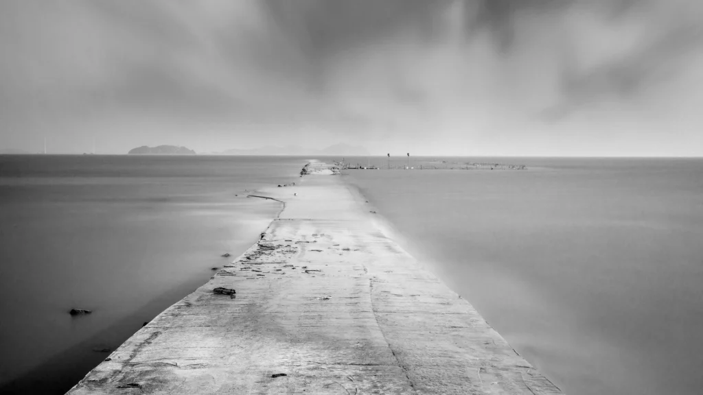 A black and white image of a track running through water and fading to the horizon.